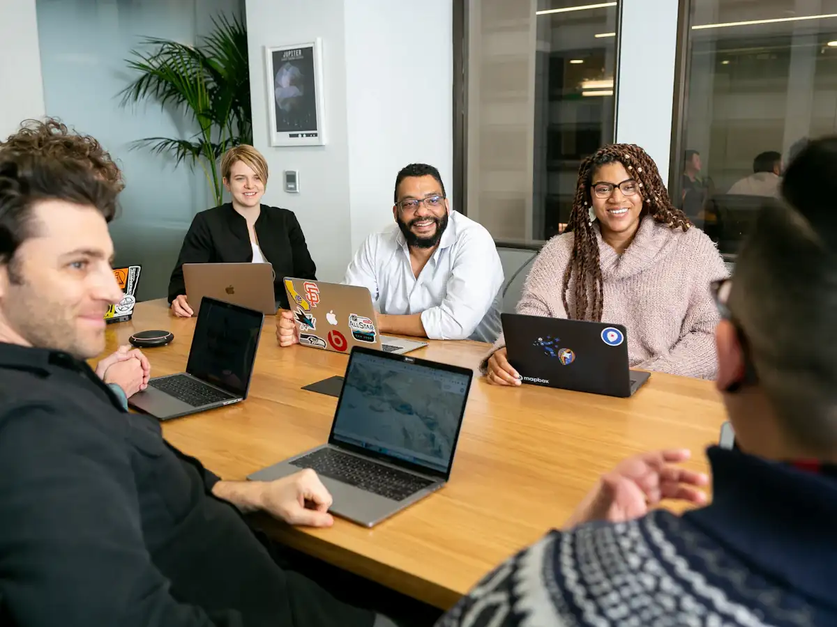 Four consultants on laptops listening to a colleague during a stand-up