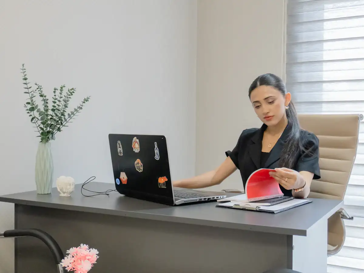 Woman working on a laptop while reading papers at a desk