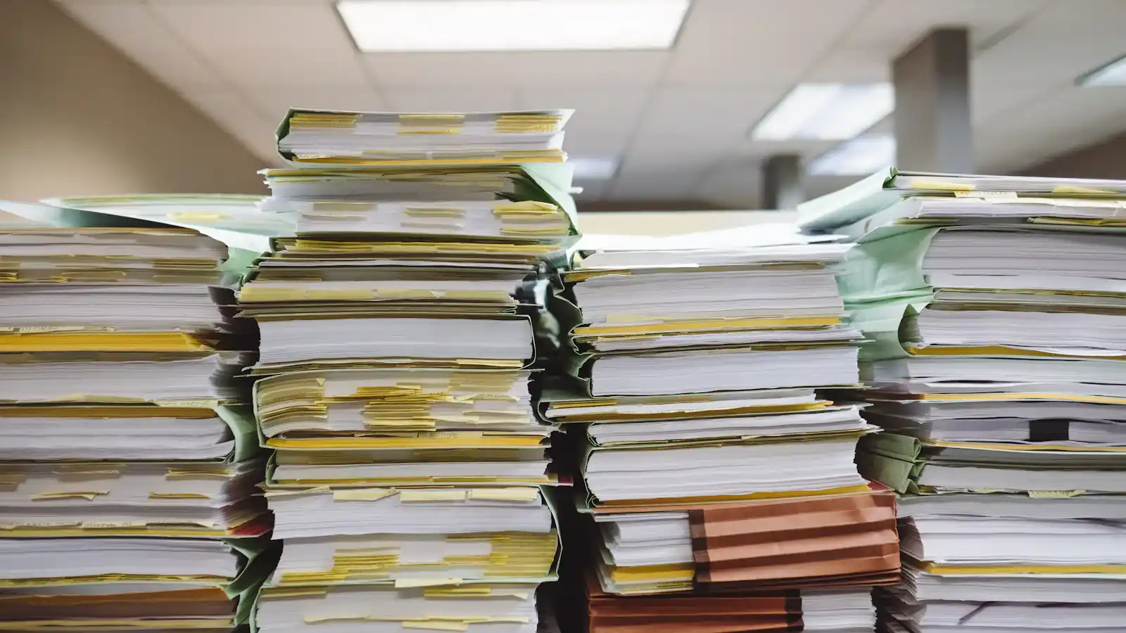 Stacks of paper documents and file folders on a desk