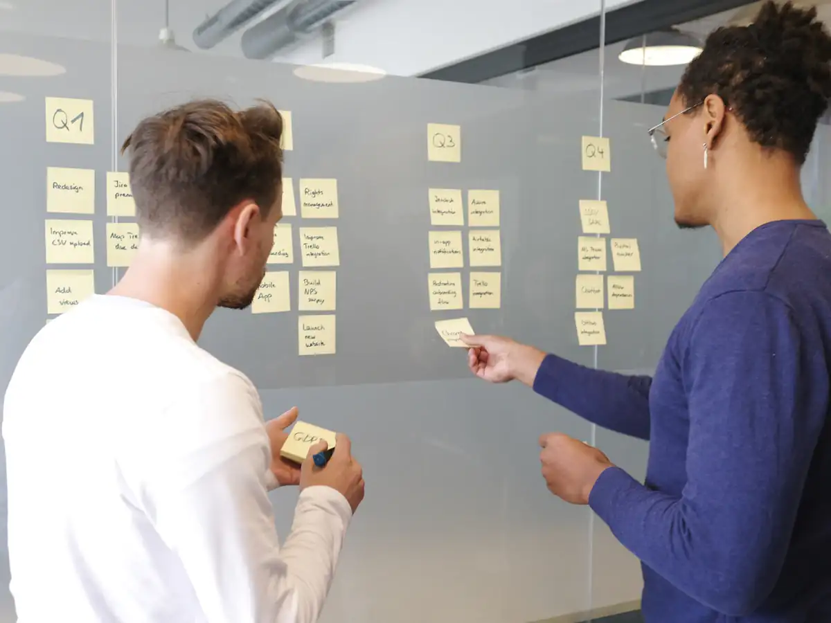 Two people planning a project with yellow sticky notes on a wall