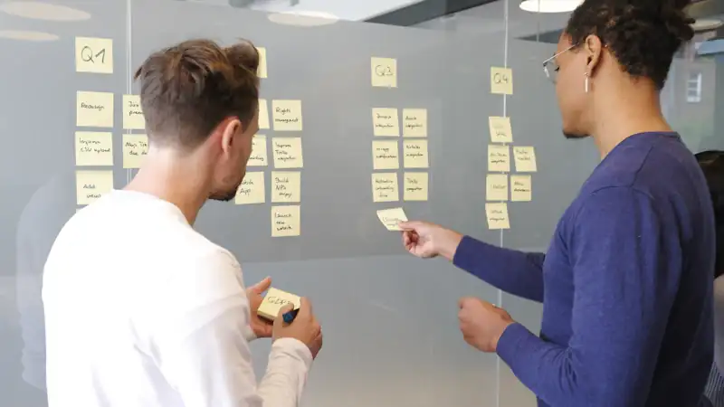 Two people planning a project with yellow sticky notes on a wall